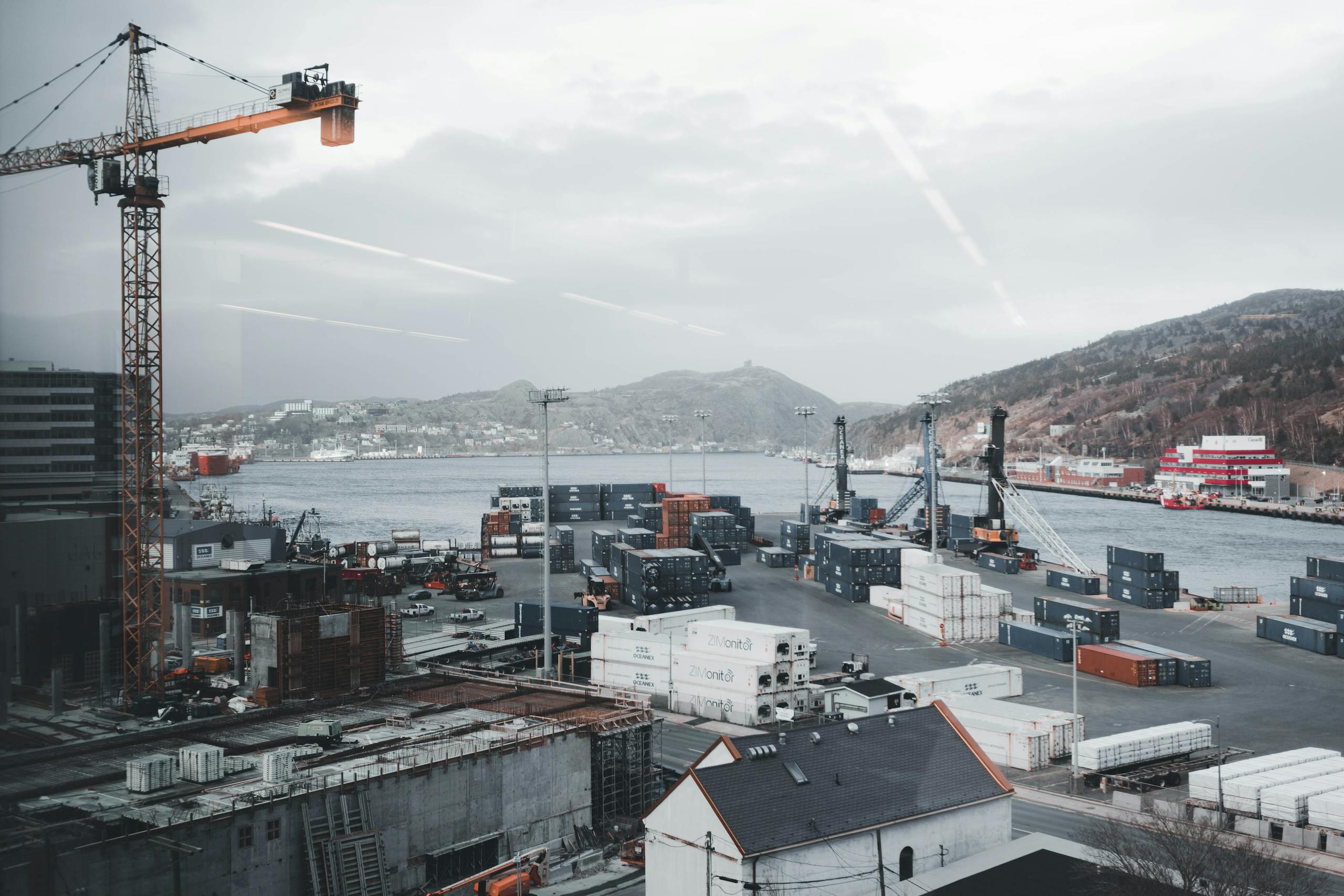 A busy industrial port with cranes and stacked shipping containers by the waterfront.