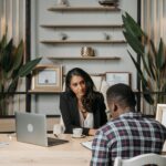 Two professionals engaged in discussion in a modern office with certificates and plants.
